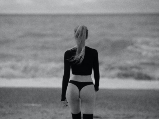 grayscale photo of a woman wearing black top at the beach