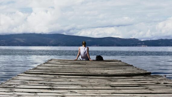 person sitting on brown wooden dock under cloudy blue sky