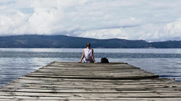 person sitting on brown wooden dock under cloudy blue sky