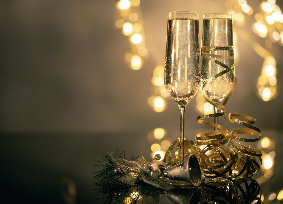 close up of two flute glasses filled with sparkling wine wuth ribbons and christmas decor