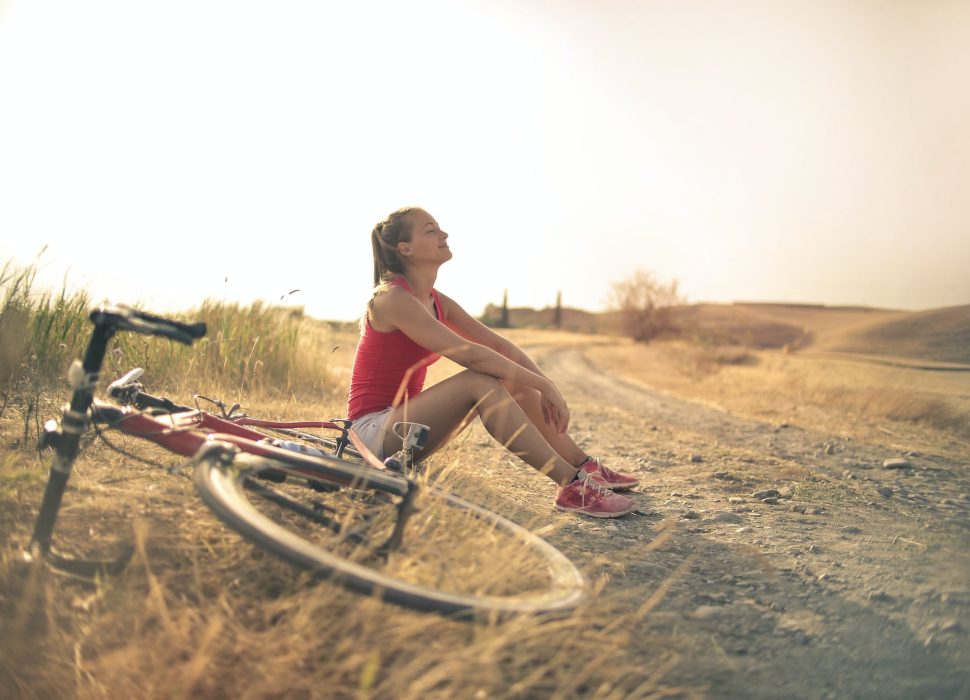 sportive woman with bicycle resting on countryside road in sunlight