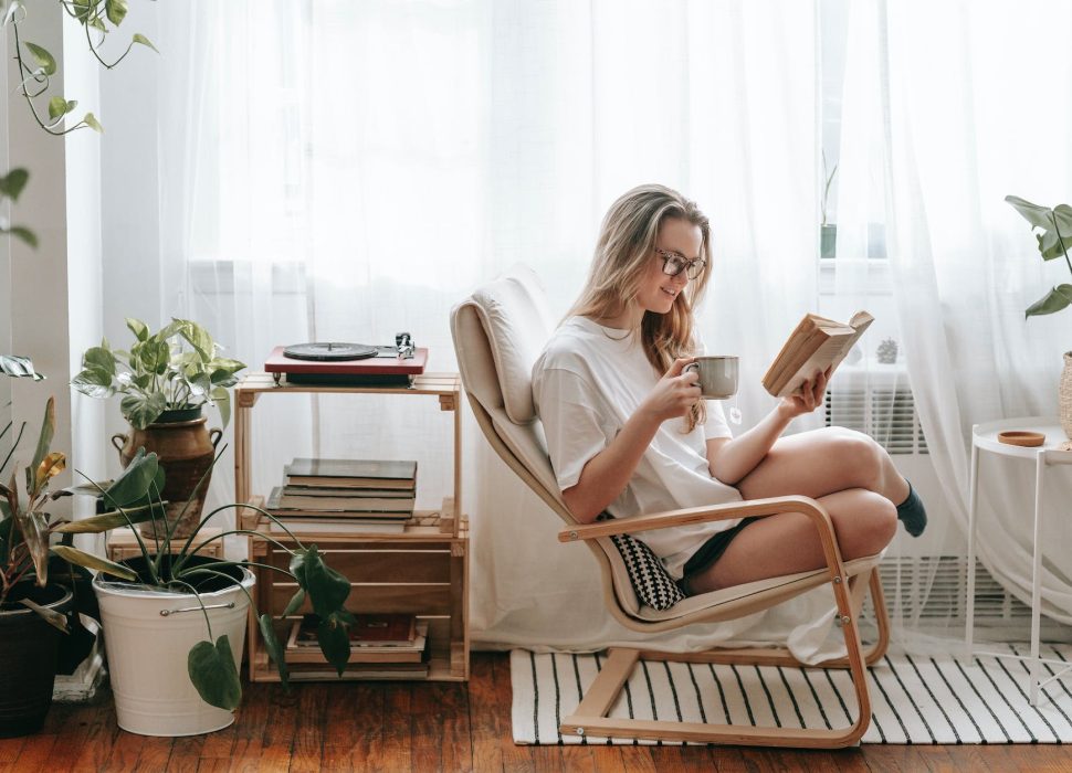 smiling woman with hot drink reading book at home